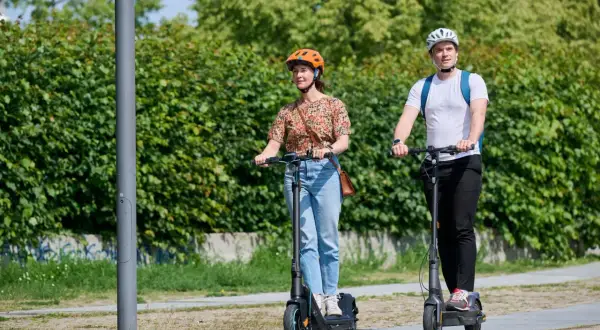 Mann und Frau fahren E-Scooter nebeneinander. Der Unterschied E-Roller und E-Scooter ist hier nicht ersichtlich, beide sind auf dem Weg.