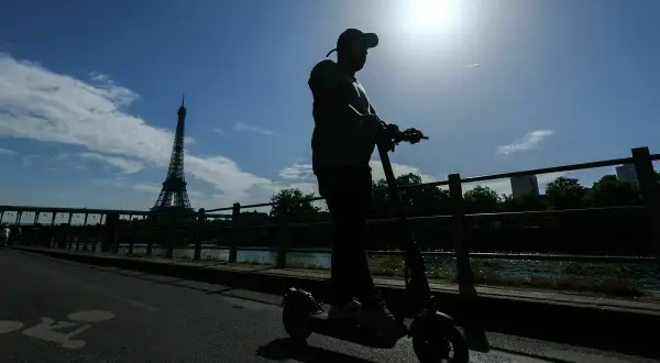 Mann fährt mit einem E-Scooter in Frankreich, die Silhouette des Eiffelturms im Hintergrund.