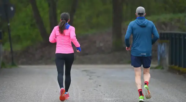 Zwei Läufer, eine Frau in Pink und ein Mann in Blau, genießen die frische Luft. Sie zeigen, was bringt joggen: Fitness und Wohlbefinden.