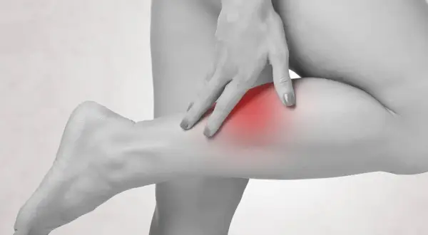 Eine Hand berührt die Wade, wo ein roter Fleck auf Schmerzen in der Wade hinweist.
