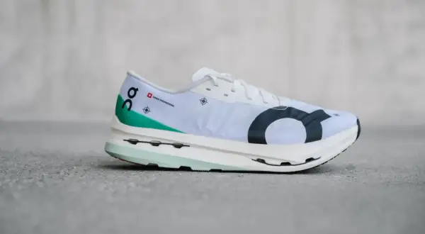 Weißer Laufschuh, On Cloudboom Echo 3, mit grünen Akzenten und schwarzem Logo.