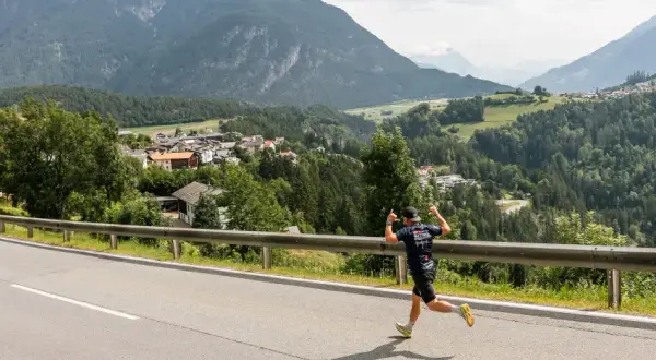 Läufer beim Pitztal Marathon mit Daumen hoch, im Hintergrund ein malerisches Bergdorf.