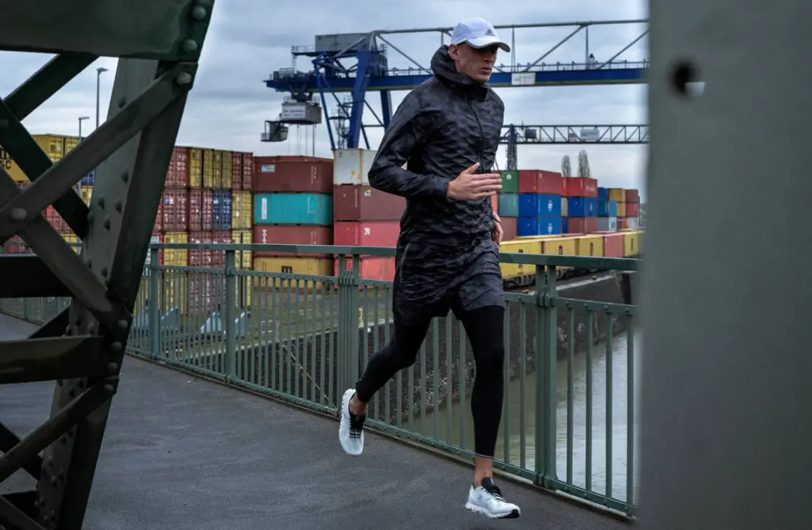 Mann joggt bei Regen über eine Brücke im Hafen. Container und Kräne im Hintergrund.