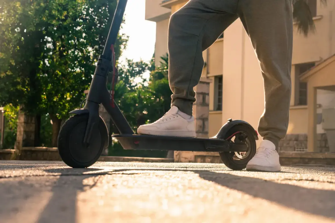 Person steht auf einem e scooter ohne kennzeichen, bereit für die Fahrt im warmen Sonnenlicht.