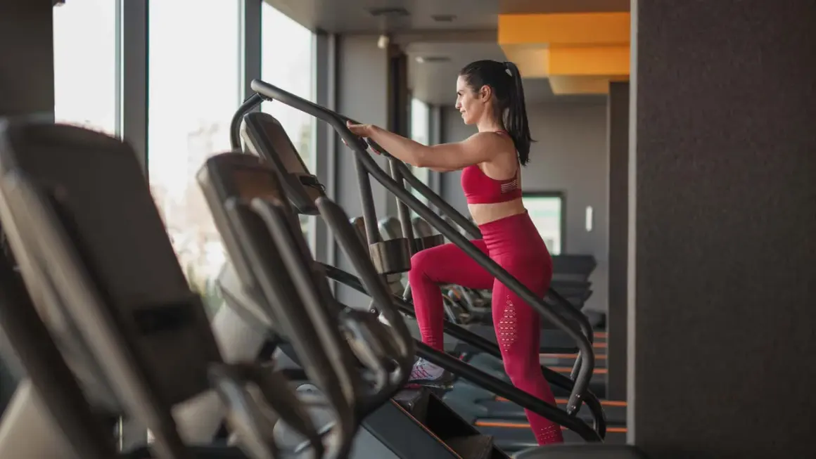 Frau im Fitnessstudio macht ein Stairmaster Workout. Sie trägt ein rotes Sport-Outfit und trainiert intensiv.