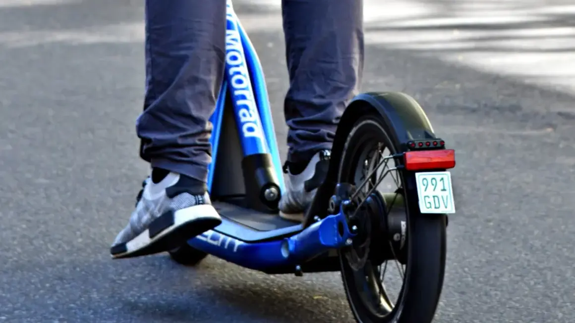 Ein e scooter fahrer auf einem blauen Roller mit dem Schriftzug "Motorrad" und einem Kennzeichen.