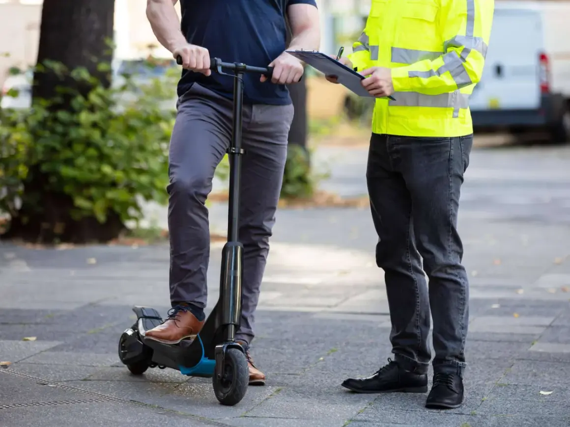 Mann auf e-scooter in Spanien, während ein anderer Mann mit Warnweste Notizen macht.