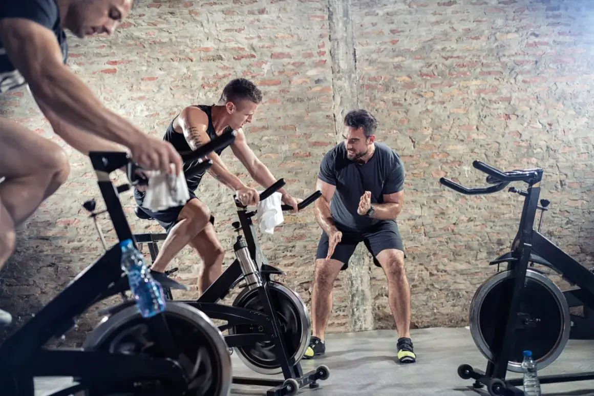 Männer trainieren intensiv beim Spinning. Ein Trainer motiviert die Sportler, die auf ihren Rädern strampeln.