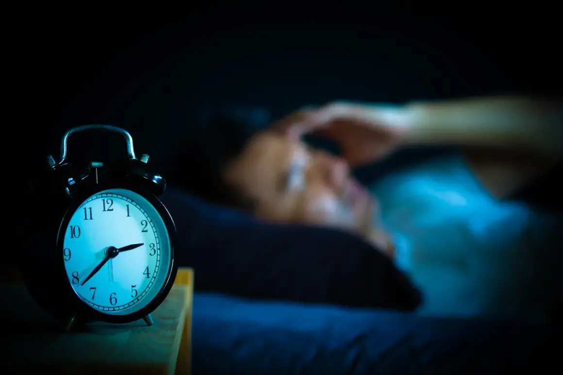 Ein Wecker zeigt 3 Uhr. Eine Person liegt im Bett, die Hand an der Stirn, und fragt sich: warum wache ich immer um 3 Uhr auf?