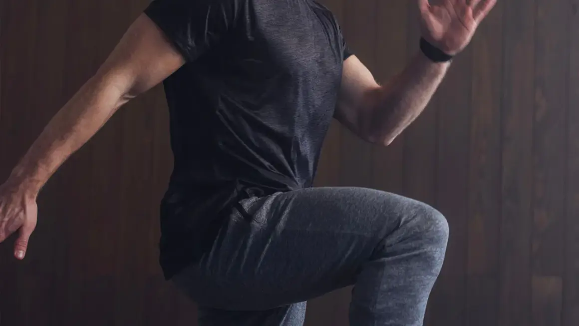 Mann in Sportkleidung, der auf der Stelle läuft, mit erhobenem Knie und ausgestrecktem Arm.