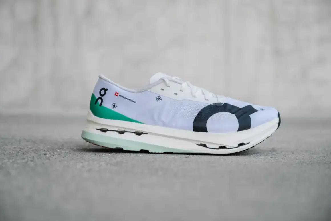 Weißer Laufschuh, On Cloudboom Echo 3, mit grünen Akzenten und schwarzem Logo.