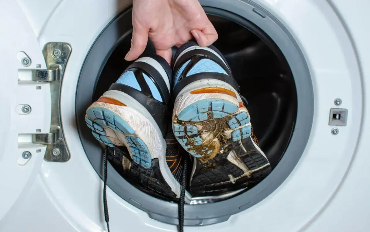 Schmutzige Laufschuhe werden in eine Waschmaschine gegeben.