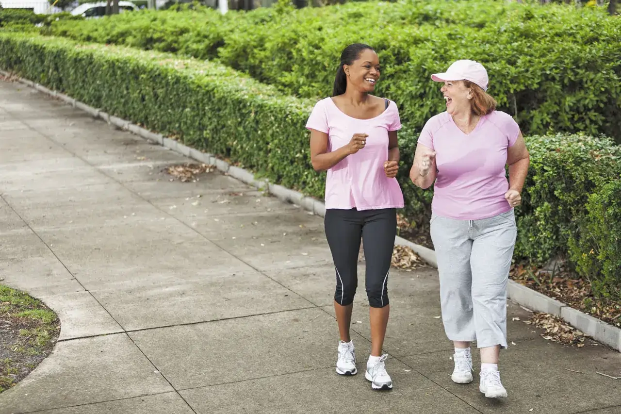 Zwei Frauen in pinken Shirts genie&szlig;en einen japanischen Spaziergang im Freien, lachen und bewegen sich auf einem Gehweg.