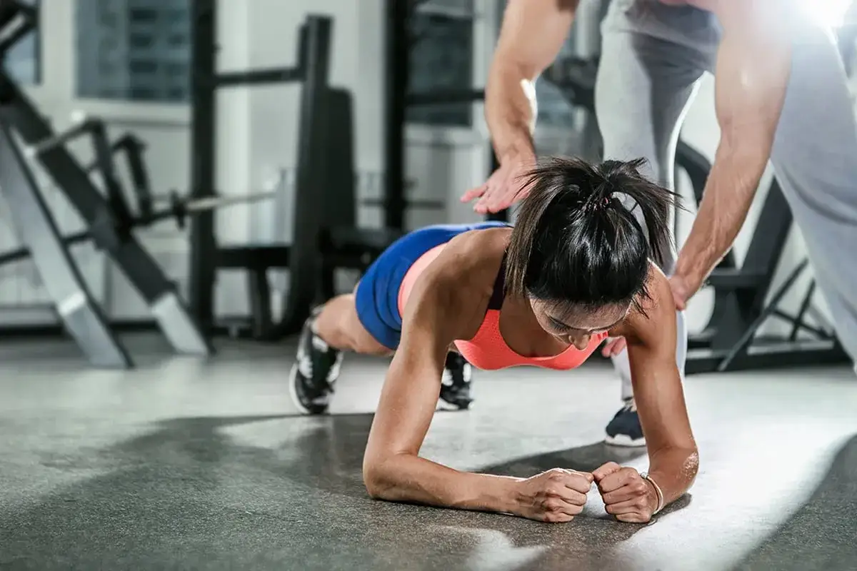 Frau im Plank-Training, ihr Trainer gibt ihr Halt.