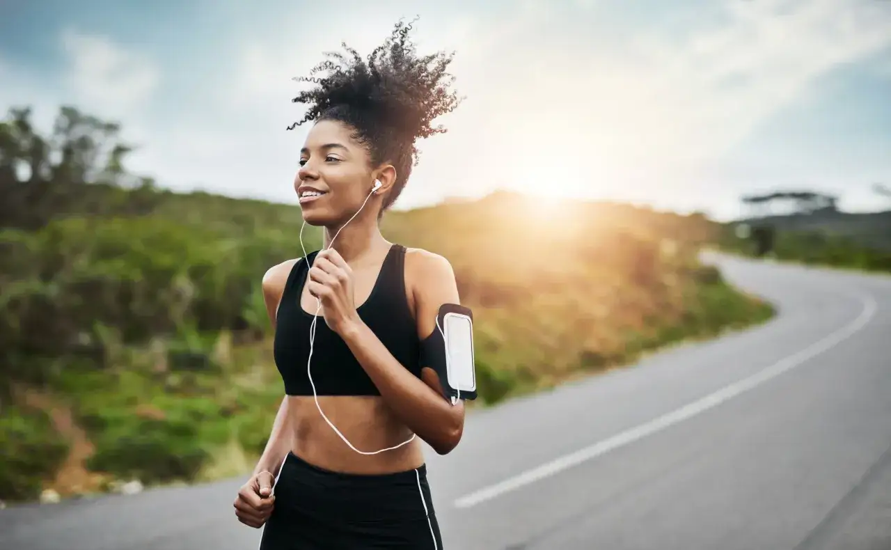 Frau mit Kopfhörern läuft auf einer Straße, die Sonne scheint. Perfekte Musik zum Laufen für ein Workout im Freien.