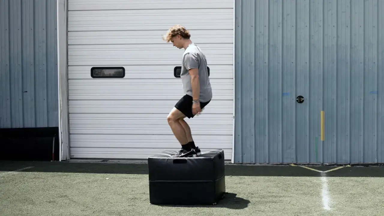 Junger Mann macht Box Jumps auf einer schwarzen Box vor einer Garage.