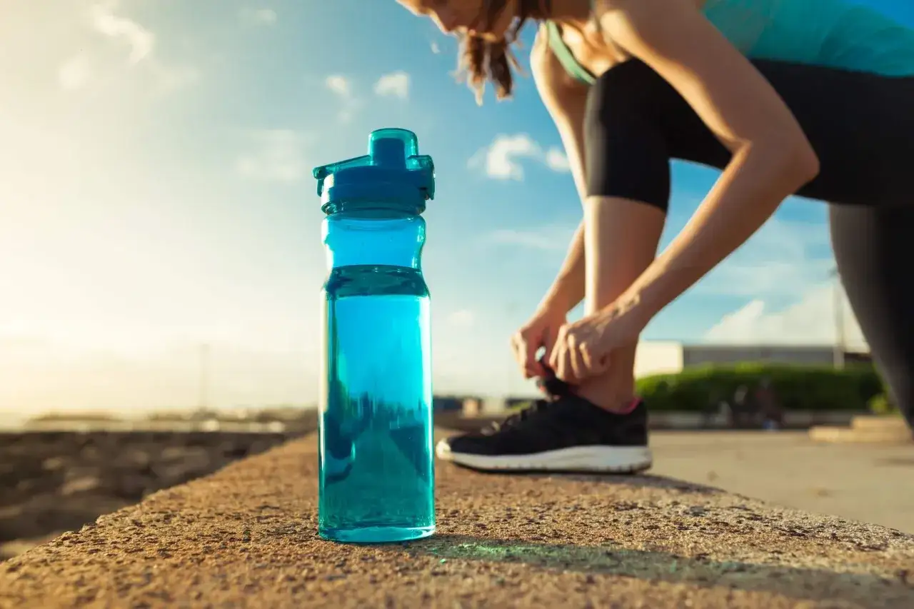 Frau schn&uuml;rt Laufschuhe, blaue Wasserflasche daneben. Ein guter Start in den Tag, auch nach Alkohol am Vorabend.