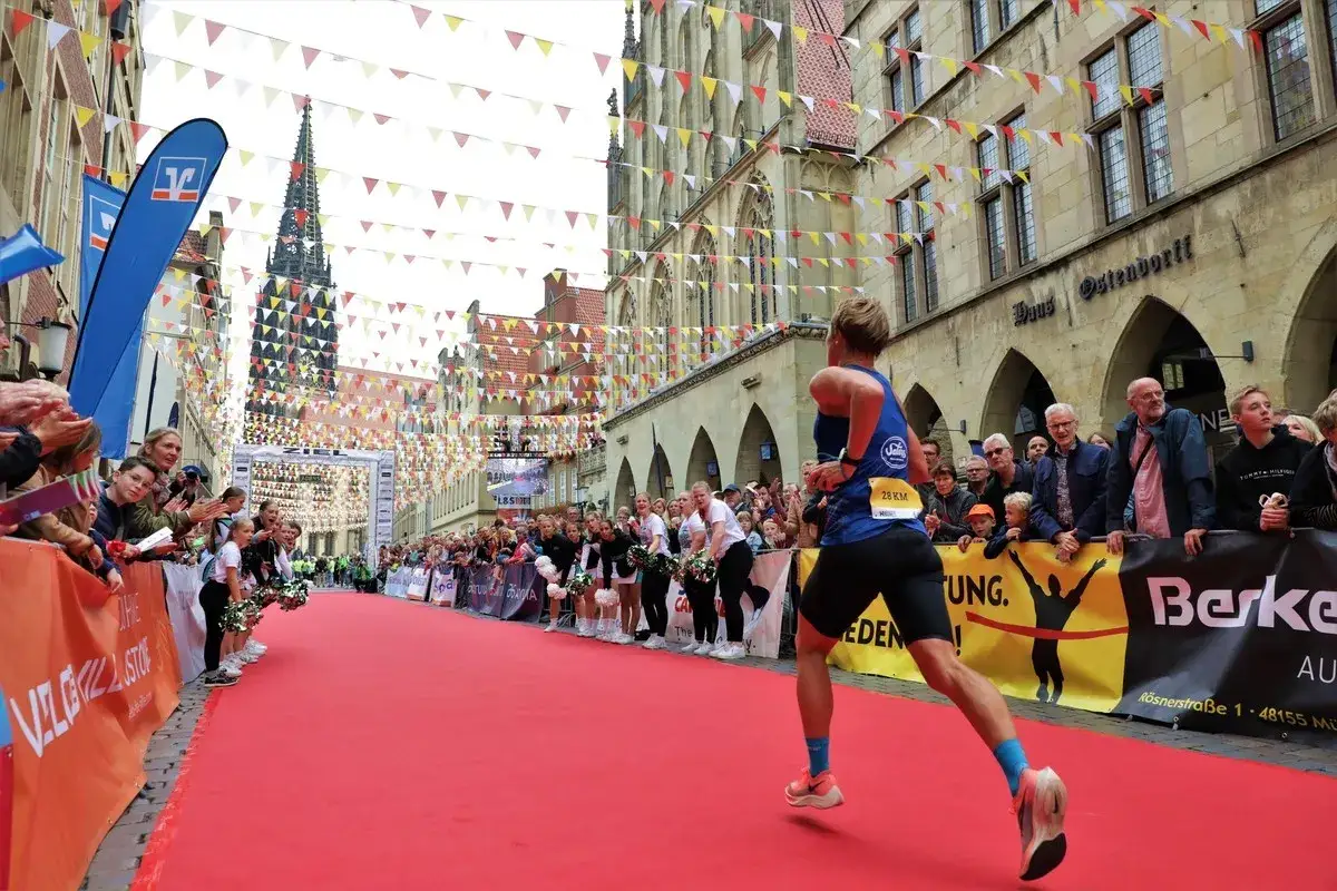 Läufer auf rotem Teppich, jubelnde Menge, Zielbogen und Fahnen. Ein Moment aus dem Marathon Kalender.