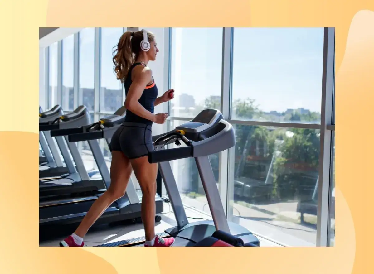 Frau mit Kopfh&ouml;rern absolviert ein intensives Laufband Training im Fitnessstudio, mit Blick auf die Stadt.
