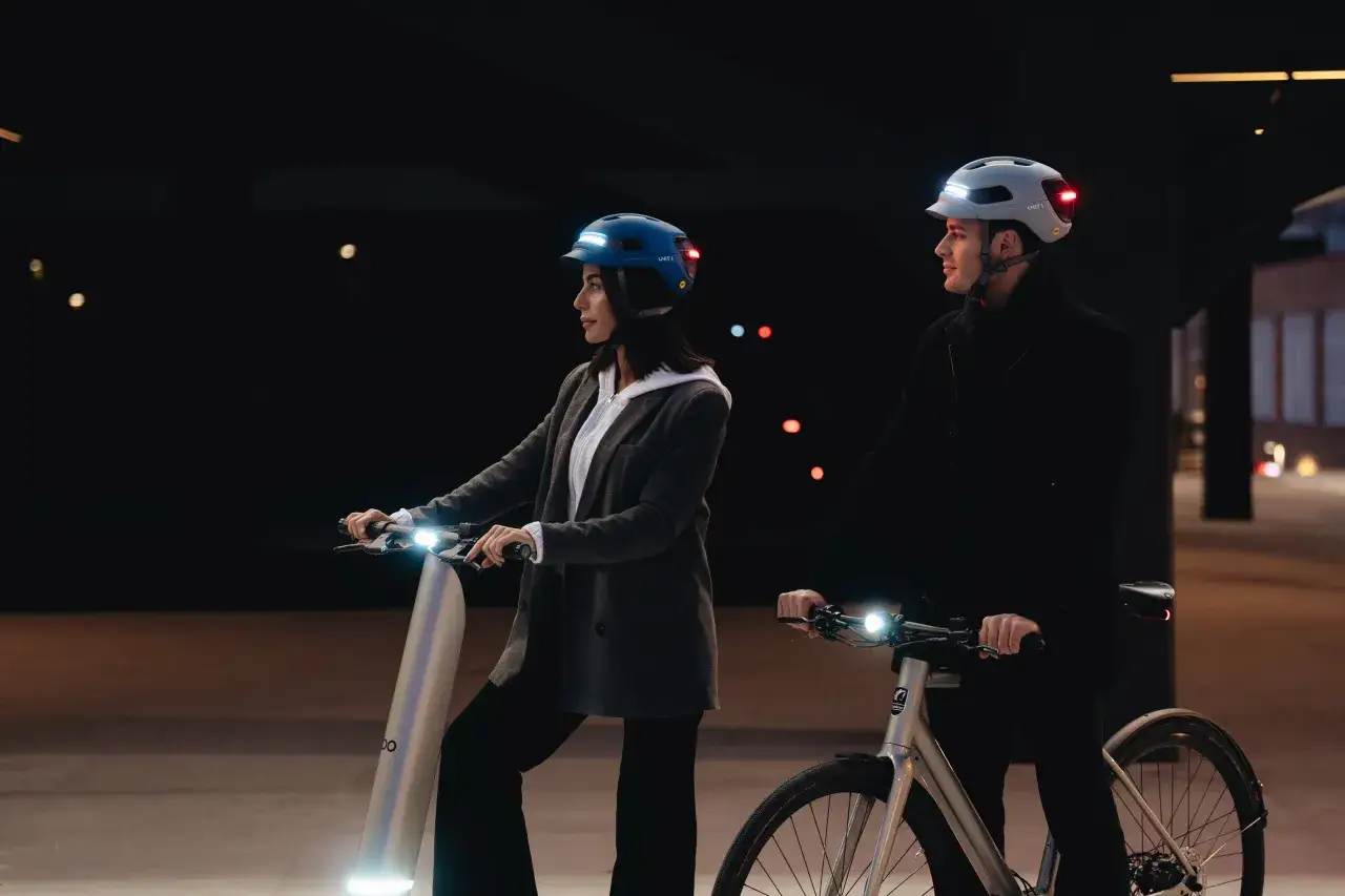 Zwei e-scooter fahrer mit leuchtenden Helmen und Fahrzeugen in der Dämmerung.