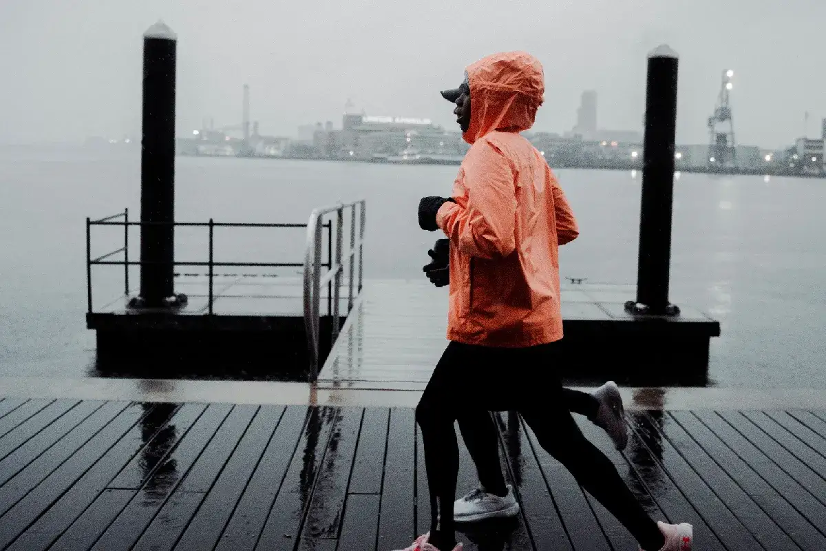 Person läuft im Winter bei Regen auf einem nassen Holzsteg. Die orangefarbene Jacke schützt vor der Kälte.