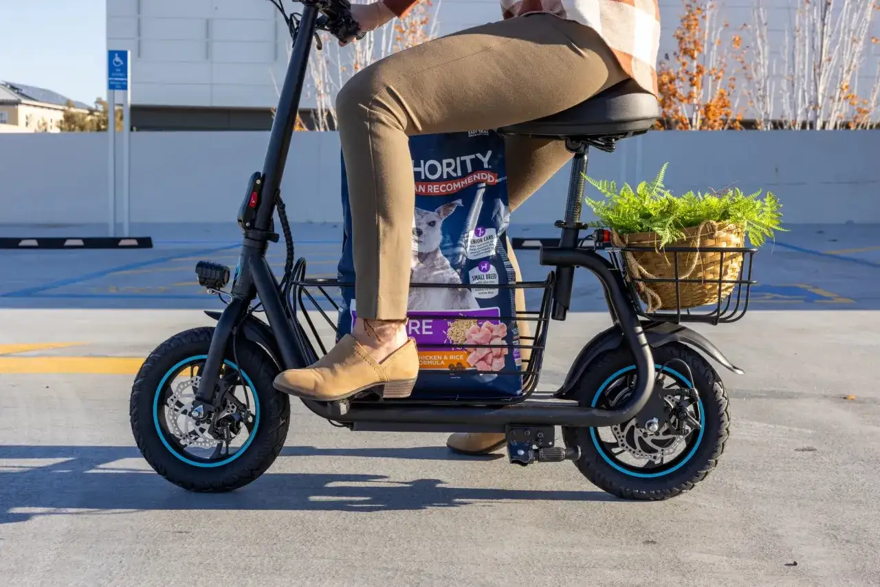 Person fährt mit einem Scooter, der eine Hundefuttertüte und Pflanzenkorb transportiert. Was ist ein Scooter? Ein praktisches Gefährt für den Alltag.