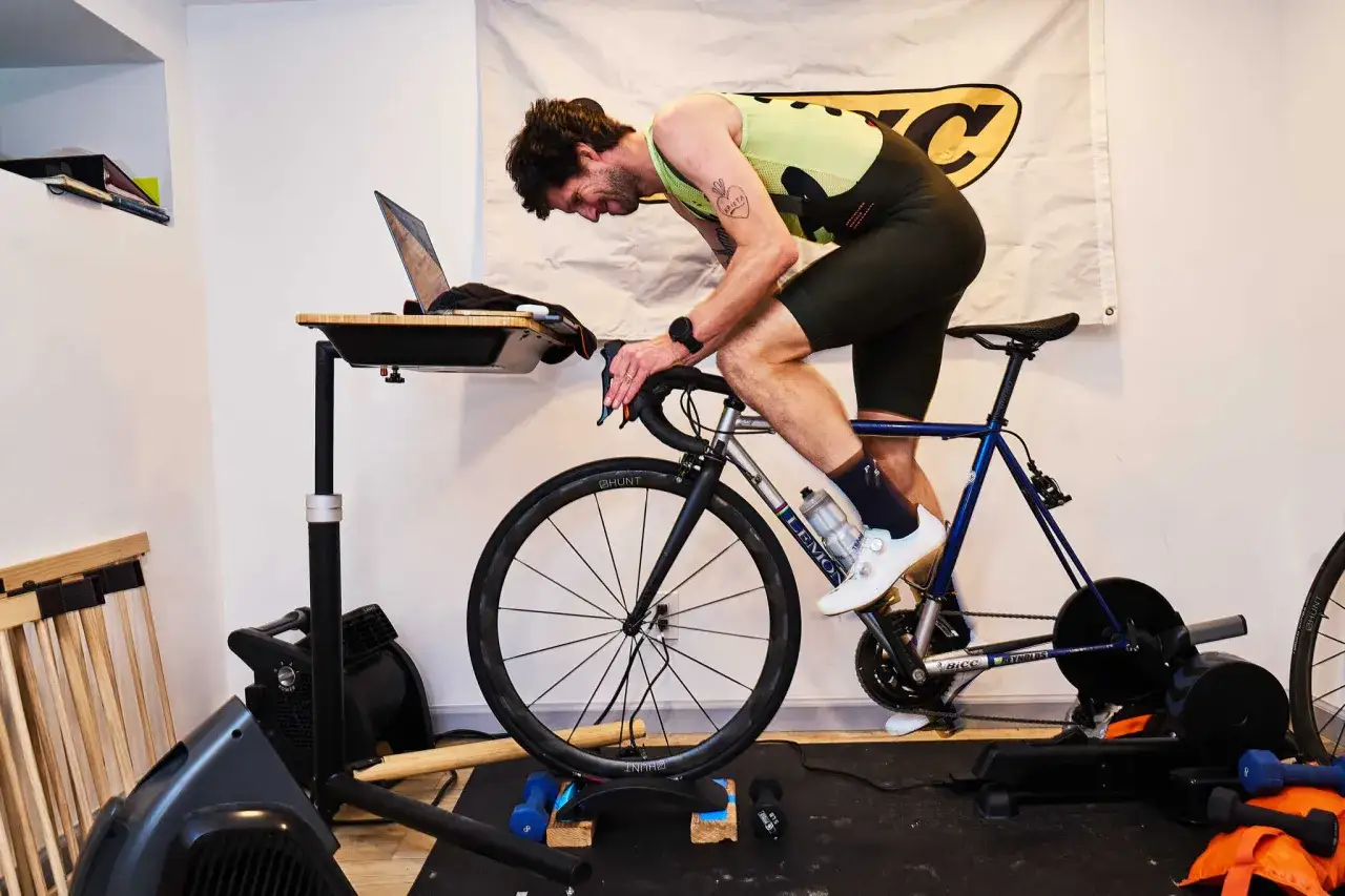 Mann auf einem Heimtrainer, der intensiv spinning macht, mit Laptopschreibtisch und Ventilator.