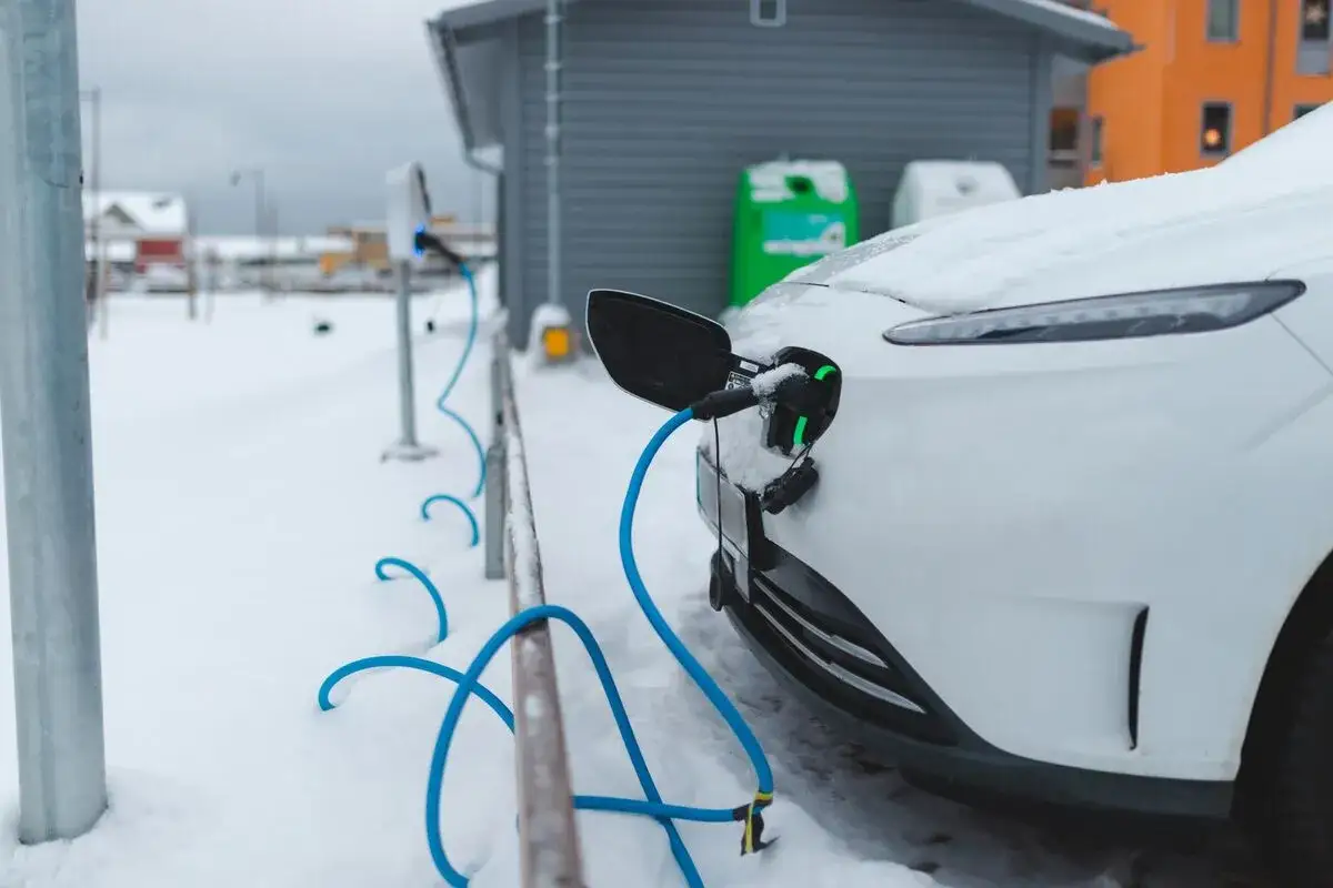 Wei&szlig;es Elektroauto l&auml;dt im Schnee. Die Ladebuchse leuchtet gr&uuml;n, was auf eine optimale Akku-Temperatur beim Laden hindeutet.