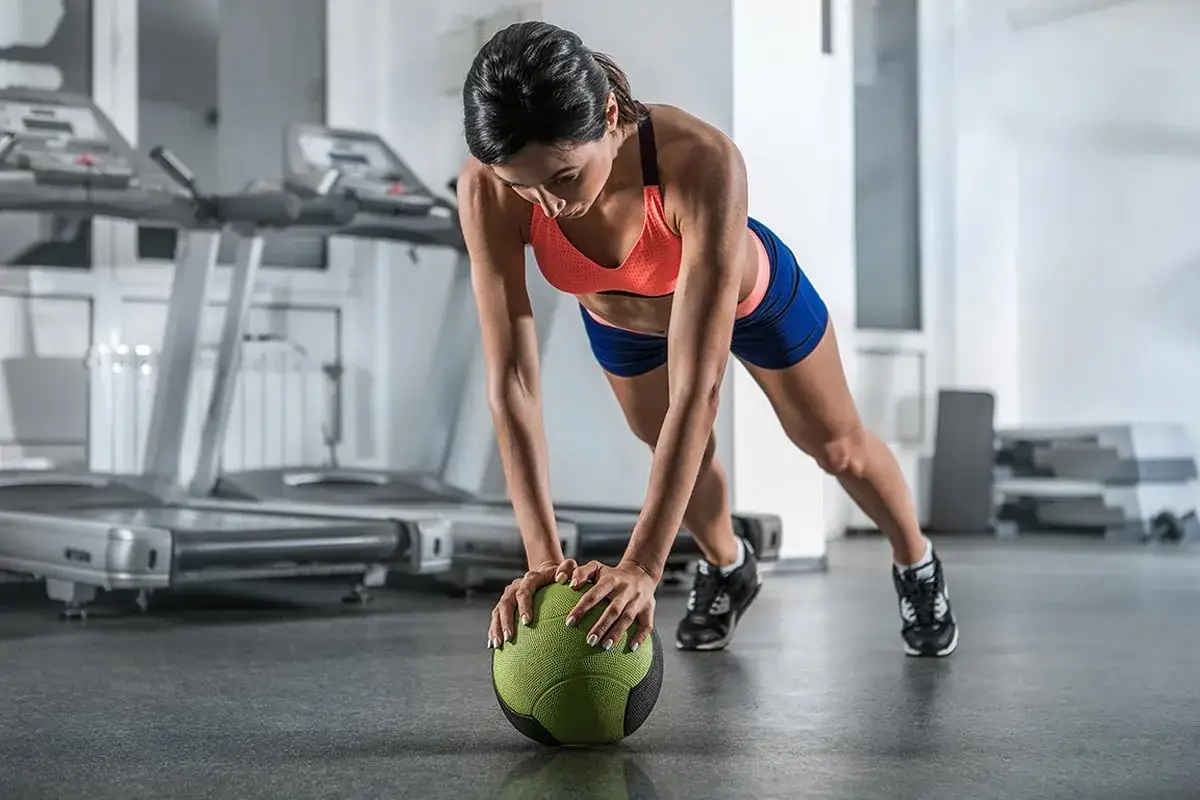 Frau in Sportkleidung macht Liegest&uuml;tze mit einem Medizinball f&uuml;r ein intensives core workout im Fitnessstudio.