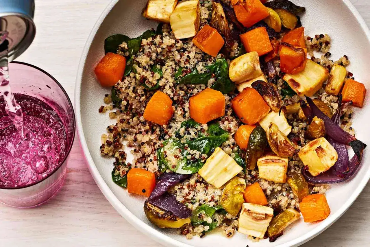 Buntes Quinoa-Gericht mit ger&ouml;stetem Gem&uuml;se wie K&uuml;rbis und Pastinaken, ein gesundes, proteinreiches Abendessen. Daneben wird ein pinkes Getr&auml;nk eingeschenkt.