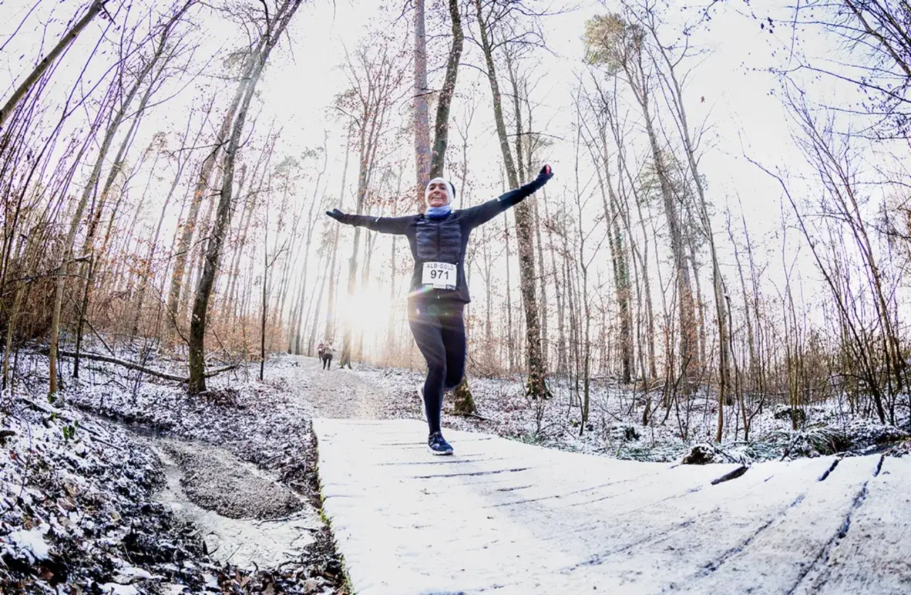 L&auml;uferin mit Nummer 971 jubelt nach erfolgreichem Lauf im verschneiten Wald. Ein Trainingsplan Laufen 10 km k&ouml;nnte sie hierher gef&uuml;hrt haben.