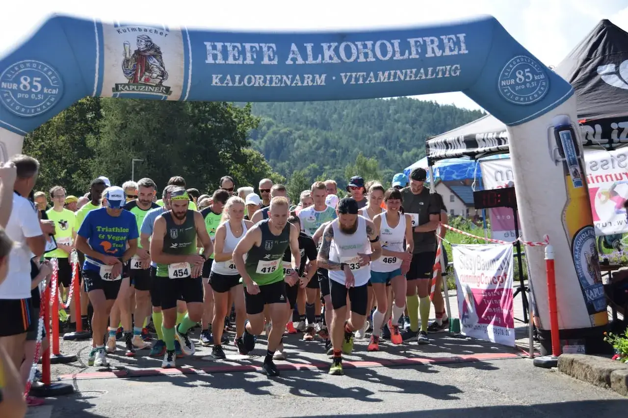 L&auml;ufer am Start des Plankenfelser Waldlaufs unter einem Torbogen mit Bierwerbung.