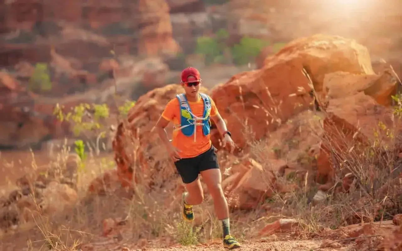 Ein L&auml;ufer in orangefarbenem Shirt und roter Kappe meistert einen steinigen Pfad. Das ist die Essenz dessen, was ist ein ultramarathon: Ausdauer in extremer Natur.