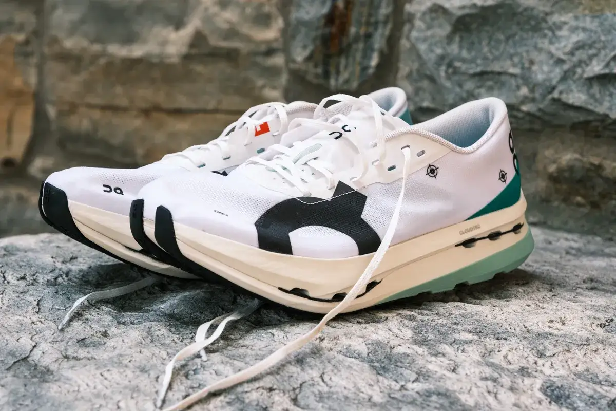 Wei&szlig;e Laufschuhe, die Cloudboom Echo 3, mit schwarzen und gr&uuml;nen Akzenten, ruhen auf Steinen.