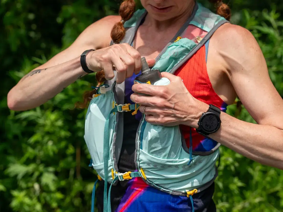 Läuferin öffnet Trinkflasche aus ihrer Laufweste. Wichtig, um beim Joggen Wasser mitzunehmen.