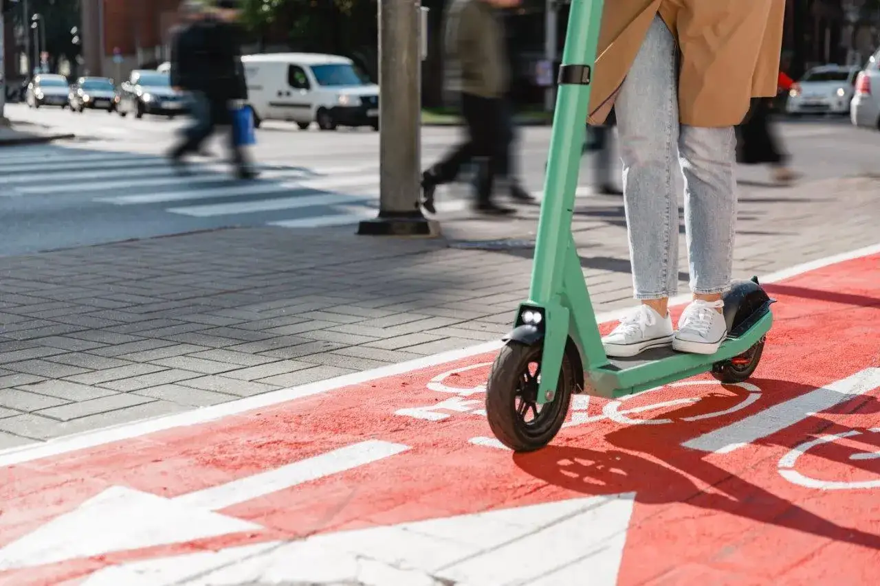 Person auf mintgr&uuml;nem E-Scooter auf rotem Radweg, bereit f&uuml;r schnelle Fahrt.