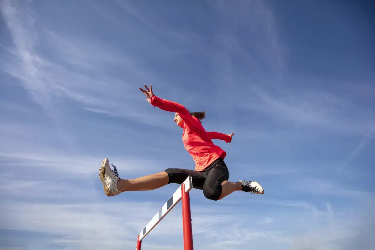 Sportlerin überquert Hürde in voller Sprungkraft, ein Beispiel für dynamisches plyometrisches Training unter blauem Himmel.