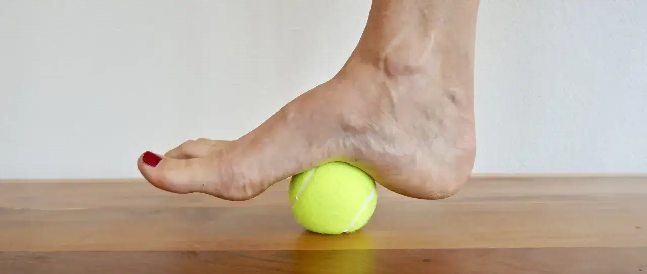 Fuß auf einem Tennisball zur Linderung von Fersensporn. Eine einfache Übung, die bei Fersensporn hilft.