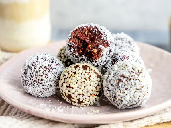 Leckeres energy balls rezept: Schokoladige Kugeln mit Kokosraspeln und Sesam auf einem Teller.