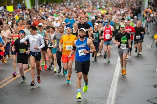 Läufer beim Halbmarathon Europa. Viele Teilnehmer in bunten Trikots, einige mit Startnummern, kämpfen sich über die nasse Straße.