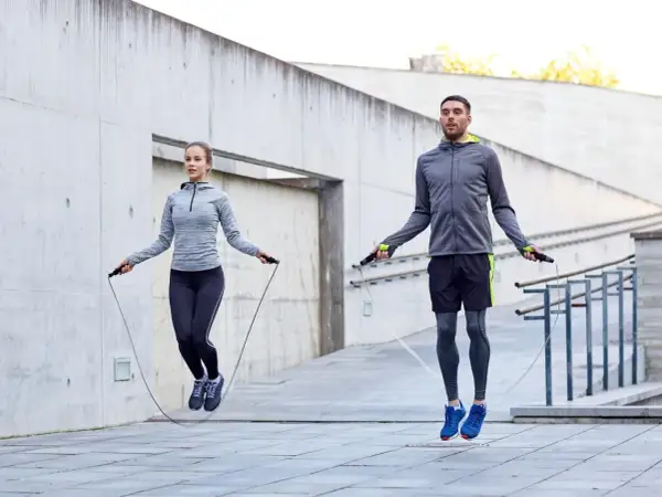 Ein Mann und eine Frau springen Seil. Sie trainieren draußen und zeigen, wie effektiv ist seilspringen für die Fitness.