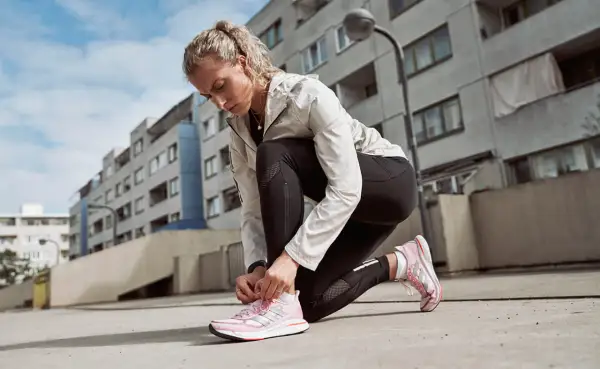 Läuferin kniet am Boden und bindet ihre neuen, pinken Laufschuhe ein. Perfekt zum Einlaufen!