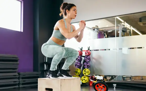 Frau macht einen Box Jump, eine Übung des plyometrischen Trainings, im Fitnessstudio.
