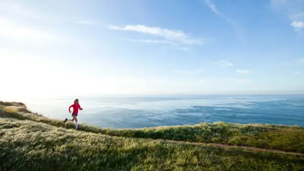 Läuferin auf Küstenpfad, trainiert für Marathon unter 4 Stunden. Weite See und Himmel.