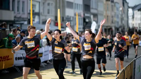 Läufer feiern Zieleinlauf beim Marathon. Ein Mann und zwei Frauen mit Startnummern, die Teil des Marathon Kalenders sind, jubeln.