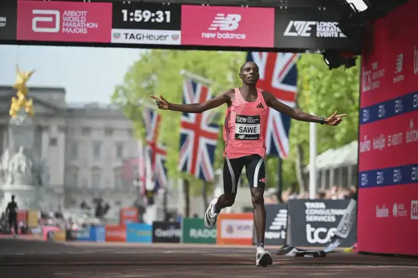 Läufer Sawe überquert die Ziellinie, vielleicht ein neuer weltrekord 5km. Britische Flaggen wehen im Hintergrund.