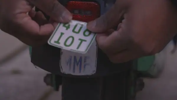Hände befestigen ein neues e-scooter nummernschild mit der Aufschrift "408 10T" über einem alten, abgenutzten Kennzeichen.