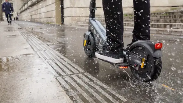 Ein e-scooter bei regen spritzt durch Pfützen auf dem nassen Gehweg.
