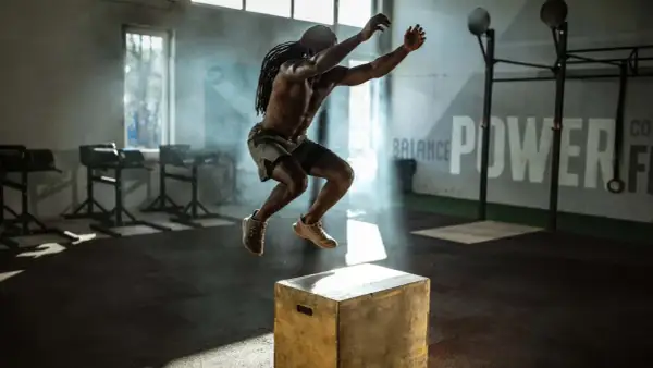 Mann macht explosive Box Jumps in einem Fitnessstudio. Rauch und Lichteffekte unterstreichen die Dynamik.