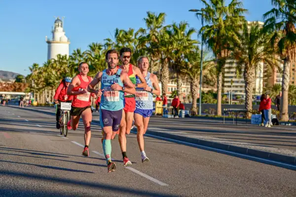 Läufer beim Malaga Marathon, vorbei an Palmen und dem Leuchtturm.